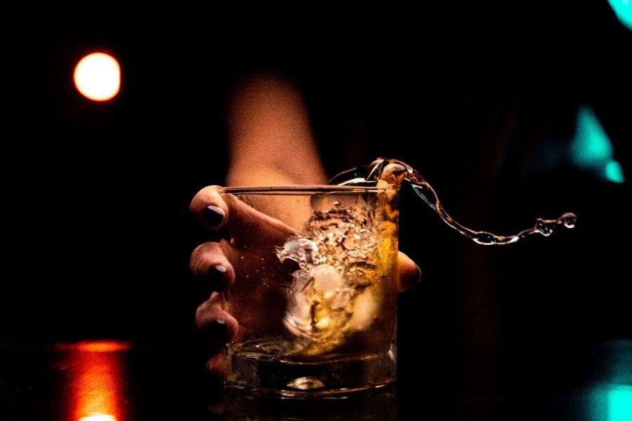 Kobieca ręka z impetem stawia szklankę z alkoholem na stół, płyn się rozlewa.